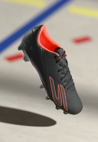 Black soccer cleat with textured upper, orange accents, and laces. Features a streamlined design and molded sole for traction.