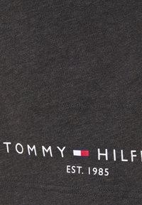 Tummanharmaa puuvillapaita, jossa on valkoiset tekstit "TOMMY HILFIGER EST. 1985" ja punainen sekä sininen logokoristus keskellä. Pehmeä tekstuuri.