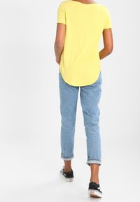 Gul kortärmad skjorta med rundad halsringning, kombinerad med ljusblå jeans, uppvikta vid anklarna, och svarta sneakers.