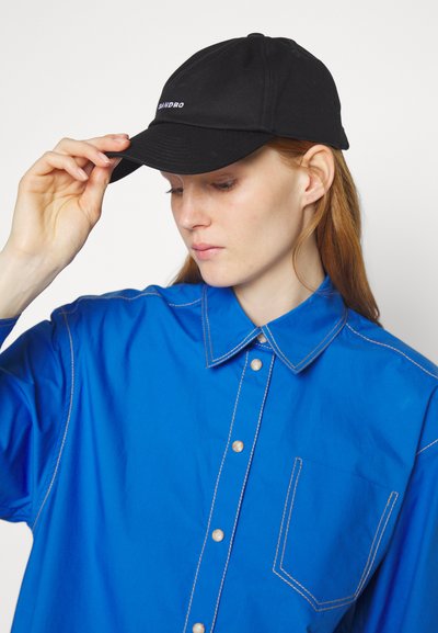 Μαύρο καπέλο μπέιζμπολ με καμπυλωτό γείσο και κεντημένο λογότυπο. Φοριέται με ένα φωτεινό μπλε πουκάμισο με κουμπιά που διαθέτει αντίθετη ραφή.