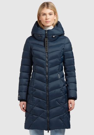 Cappotto imbottito blu navy con cuciture a forma di chevron, colletto alto e zip completa. Presenta una patch con logo sulla manica e tasche laterali. Tessuto liscio.