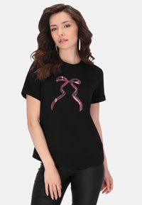 Sort t-shirt med korte ærmer, der har et pink glitrende sløjfedesign i midten. Blødt, glat stof med en afslappet pasform.