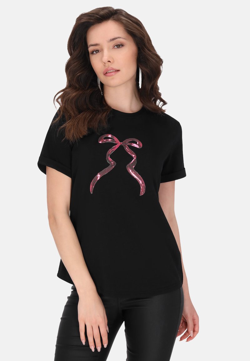 Sort t-shirt med korte ærmer, der har et pink glitrende sløjfedesign i midten. Blødt, glat stof med en afslappet pasform.