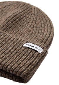 Brun ribbet beanie lavet af uld, med en foldet skygge og et hvidt mærke med sort tekst. Blød tekstur med et varmt, hyggeligt udseende.