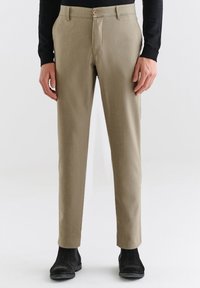 Beżowe spodnie z dopasowanym krojem, o gładkiej fakturze, z kieszeniami z przodu i z zapięciem na guzik, zestawione z czarnymi botkami za kostkę.