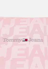 Różowa teksturowana powierzchnia z logo "Tommy Jeans". Tło przedstawia powtarzający się wzór "JEANS" o różnym stopniu przezroczystości. Logo zawiera kolorowy prostokątny akcent.