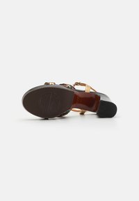Sanda negra y multicolor con tiras y tacón grueso. Cuenta con una parte superior de cuero suave y una suela de goma texturizada. Presenta detalles metálicos visibles.