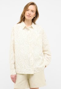 Light beige button-up shirt with a leaf pattern, long sleeves, and a chest pocket. Paired with light beige shorts. Smooth texture.