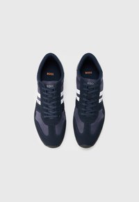 Baskets bleu marine avec une tige en tissu texturé, présentant deux rayures blanches, un bout rond et des lacets plats. Marque sur la languette et le côté.