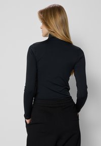 Zwarte langmouw turtleneck top gemaakt van een gladde, stretchy stof, met een aansluitend ontwerp en een hoge hals.