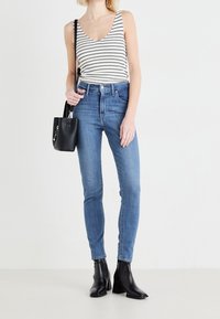 Top de rayas, sin mangas, en blanco y negro; vaqueros de denim azul de tiro alto y corte ajustado; botines negros con tacón; bolso negro pequeño.