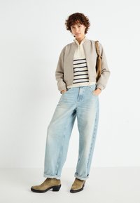 Beige bomber jacket over a striped, cream sweater. Loose light blue jeans and olive ankle boots with a black sole. Simple, casual outfit.