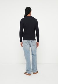 Pulover tricotat navy cu model cu nervuri, cu mâneci lungi, asortat cu blugi denim de culoare albastru deschis, având buzunare la spate. Modelul este văzut din spate.