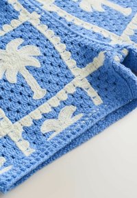 Tissu bleu crocheté avec motifs de palmiers blancs et bordures festonnées, plié sur une surface claire.