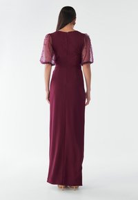 Garš burgundijas krāsas kleita ar pieguļošu siluetu. Iezīme caurspīdīgas pūkainas piedurknes, rotātas ar nelielām pērlītēm. Gluda tekstūra, grīdas garuma dizains.