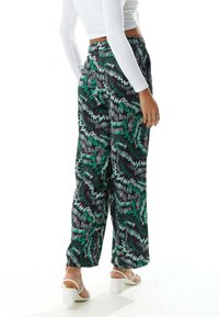 Black wide-leg pants featuring a colorful green and white abstract pattern, made from lightweight fabric, complemented by heeled sandals.