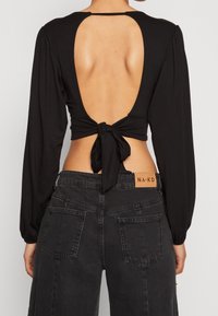 Svart långärmad topp med öppen ryggdesign, knuten vid midjan. Mjukt tyg, slät textur. Kombination med högmidjade svarta denimjeans.