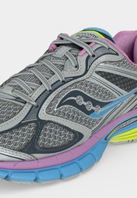 Γκρι αθλητικό παπούτσι Saucony με ροζ, μπλε και λάιμ λεπτομέρειες, λεπτομερή επάνω μέρος από δίχτυ και κορδόνια δεμένα στο πάνω μέρος.