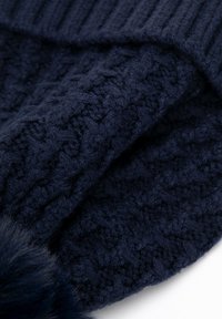 Námořnická pletená čepice s texturovaným vzorem, s žebrovaným lemem a chlupatým umělým bambulí na vrcholu pro zvýraznění detailu.