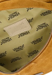 Die Innenseite der Wildleder-Handtasche ist in einem hellbraunen Farbton gehalten, mit einem Reißverschluss und einem beigen Etikett, auf dem "Venezia Genuine Leather" auf einem hellgrünen, gemusterten Futter steht.