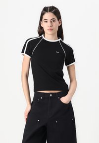 Svart kortärmad t-shirt med vit detaljering, rund halsringning och korta ärmar. Bärs med högmidjade svarta byxor.