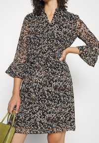 Czarna sukienka z kwiatowym wzorem w odcieniach różu, bieli i brązu. Posiada fason kopertowy, długie rękawy oraz pasek w talii.