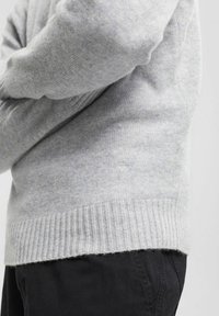 Grauer Pullover aus weichem Material, mit geripptem Saum und Bündchen. Das Design ist schlicht mit einer glatten Textur, ohne Muster oder Akzente.
