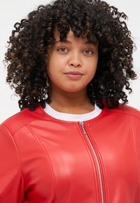 Κόκκινη δερμάτινη τζάκετ μπομπέρ με λείο υφαντό, διαθέτει λευκό γιακά και μπροστινό φερμουάρ. Εντυπωσιακές ραφές στους ώμους.