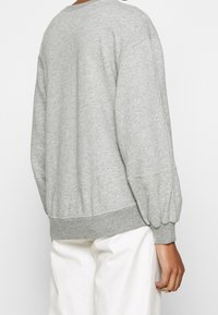 Harmaa pusero, jossa on ilmapallohihat ja resorireuna. Pehmeä koostumus ja rento istuvuus, nähtynä takaa.