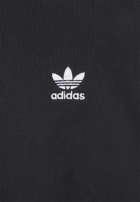 Tissu noir arborant un logo Adidas blanc avec trois bandes et un motif de feuille. Le tissu présente une texture côtelée.