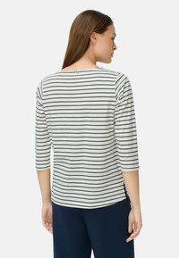 Gestreiftes Langarmshirt in Hellgrau mit Marineblau Linien, ausgestattet mit seitlichen Schlitzen und einem Knopfdetail am Rücken, aus einem weichen, strukturierten Stoff gefertigt.