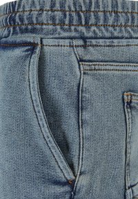 Gai zils denims, kas izceļas ar maigu tekstūru, elastīgu jostu, sānu kabatām un oranžām šuvēm.