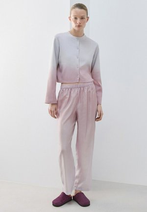 Mujer de pie con un cárdigan con botones en degradado que va de gris claro a rosa, pantalones rosas holgados y zapatos tipo mocasín de color púrpura oscuro.