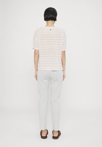 Camiseta a rayas de color rosa claro con mangas cortas y escote redondo, combinada con pantalones gris claro y sandalias marrones.