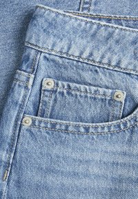 Lys blå denimjeans har en stor frontlomme, sølvnitter og kontrasterende gule stoffer, som fremhever teksturen i stoffet.