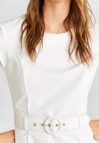 Robe blanche à manches courtes, dotée d'une ceinture ronde avec une boucle circulaire et d'une texture lisse, mettant en valeur une silhouette ajustée.