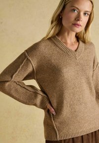 Sweter z dekoltem w serek w miękkiej brązowej mieszance wełny; ma ściągacze na mankietach i dolnym brzegu, boczne rozcięcia oraz lekko luźny krój dla wygody.