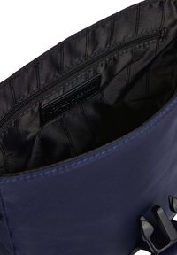 Interno di una borsa in tessuto blu navy con fodera nera, dotato di una tasca con zip e un'etichetta con il logo; include due clip laterali per la chiusura.