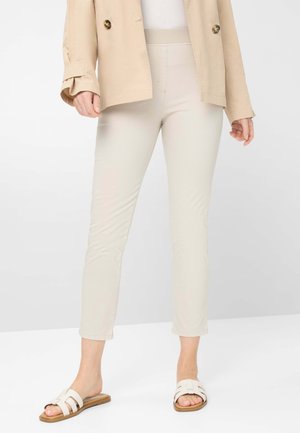 Beige Textilhose mit taillierter Passform und Knöchellänge, kombiniert mit weißen Riemenslippern mit breitem Riemen und flacher Sohle.