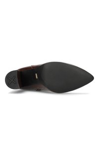 Donkerbruine leren puntige schoenzool met een gestructureerde hak die een zwart X-patroon vertoont en een klein gouden merkteken nabij de voetboog.