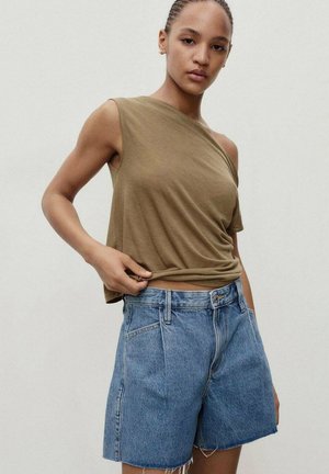 Olive green asymmetrical tank top with a relaxed fit, paired with high-waisted light blue denim shorts featuring frayed hems.