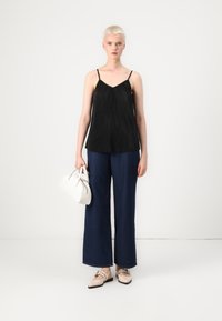 Μαύρο πλεκτό τοπάκι με λεπτές ράντες, συνδυασμένο με σκούρο μπλε παντελόνι με φαρδιά μπατζάκια. Το μοντέλο κρατά μια μικρή λευκή τσάντα χεριού και φοράει μπεζ φλατ παπούτσια.