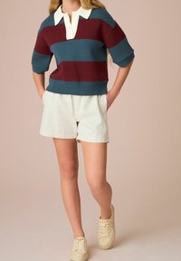 Sweter dzianinowy w paski w kolorze morskim i burgundowym z białym kołnierzem, zestawiony z kremowymi szortami w cienkie paski i jasnymi trampkami.