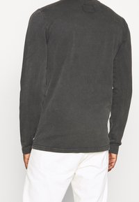 Långärmad skjorta i mörkgrått bomull med rund hals, med en fyrkantig etikett på baksidan och subtila sömnadsdetaljer.