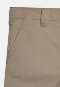 Pantalons en coton beige avec une texture lisse, présentant une coupe droite, une poche avant et des détails de couture près de la taille.