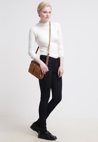 Hvit ribbet genser, marineblå stramme jeans, brun skinn crossover-veske og svarte spenne sko skaper et avslappet antrekk med kontrasterende teksturer.