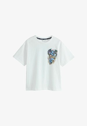 Tricou alb cu mâneci scurte, cu un mic grafic colorat al unui dragon albastru cu țepi roșii și flăcări pe zona stângă a pieptului.