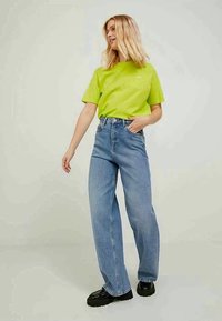 Lime roheline lühikese varrukaga T-särk, kõrge vöökohaga heledad sinised laiad püksid, mustad kandilised kingad, minimalistlik disain ja nähtavad mustrid puuduvad.