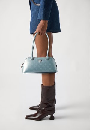 Borsa sintetica azzurro chiaro con motivo floreale a rilievo e ferramenta argentata, dotata di due manici e chiusura con zip, tenuta da una persona.