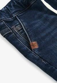 Joggers en denim bleu foncé avec une taille élastique, dotés d'une étiquette en cuir cousue avec une étoile. Texture lisse et design décontracté.